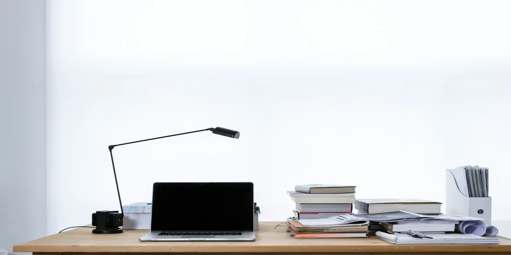 A white wall behind a computer on a desk alongside some books.